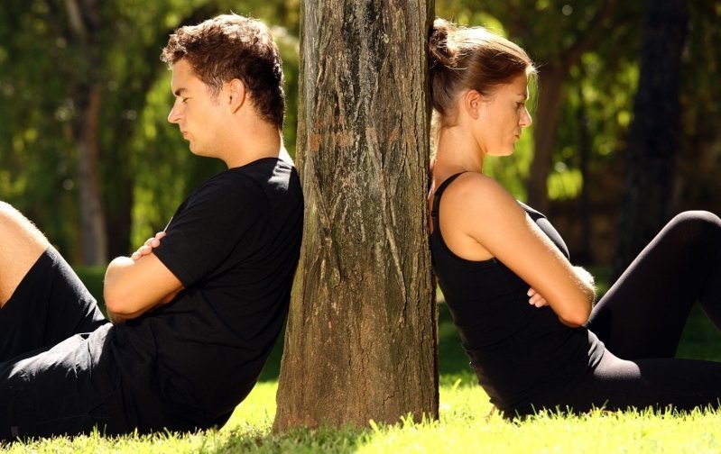 Парень и девушка сидят, прислонившись спинами к дереву