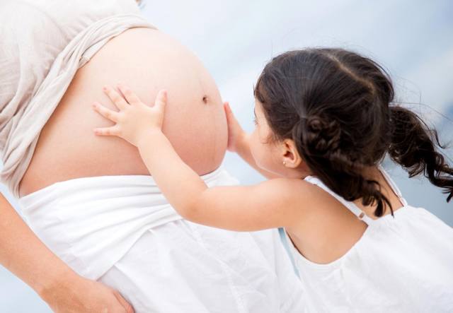 Девочка трогает живот беременной