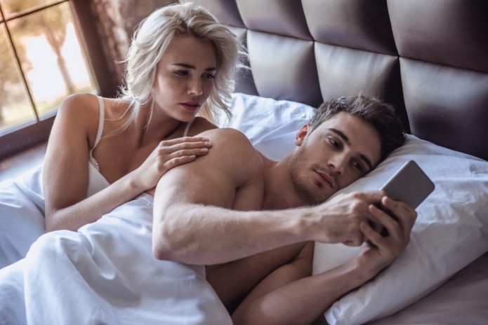 Девушка смотрит в телефон парня в кровати
