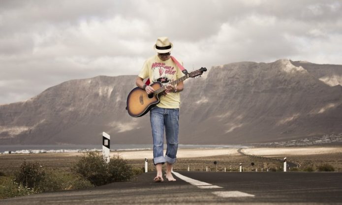 Мужчина босиком идет по дороге и играет на гитаре