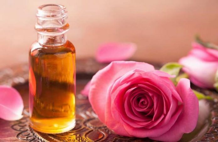 Эфирное масло розы в прозрачном флаконе и цветы