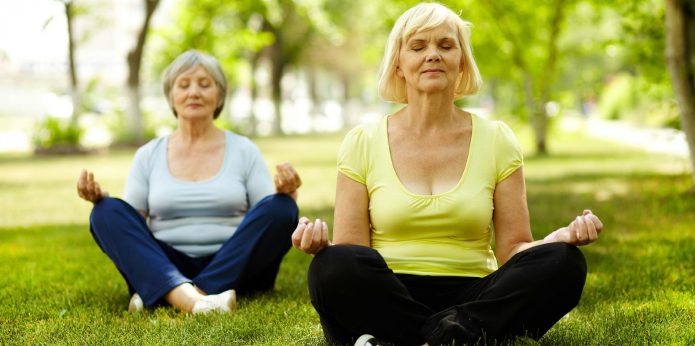 Женщины в возрасте медитируют на лужайке